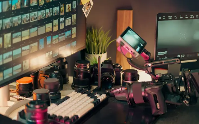 A video-production desk with cameras, lenses and two monitors, lit in warm amber.